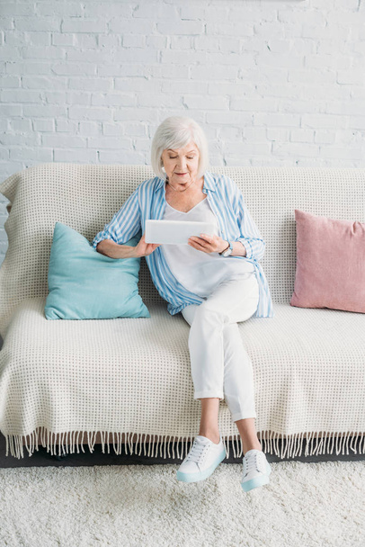 Starší žena pomocí tabletu při odpočinku na gauči doma - Fotografie, Obrázek