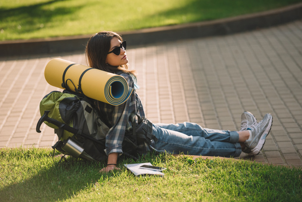 young female traveler with backpack resting on green grass at sunset - Foto, Imagem