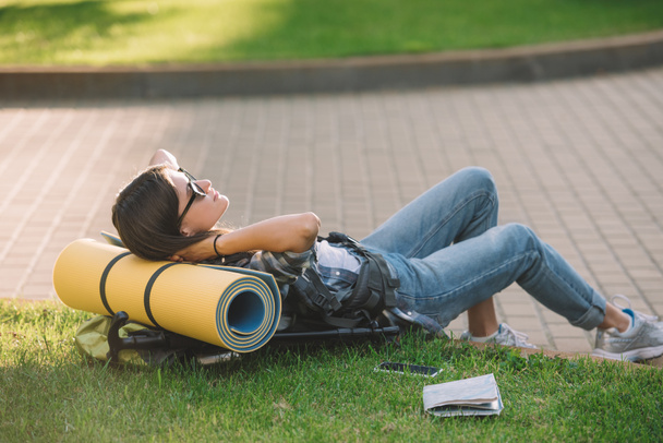 jeune femme en lunettes de soleil couché avec sac à dos sur l'herbe
 - Photo, image