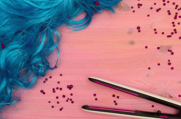 Blue long hair (wig) and hair iron (straightener) on purple wooden desk table background. - Фото, изображение