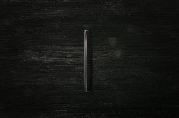 Black plastic hair comb isolated on black wooden background.  - Zdjęcie, obraz