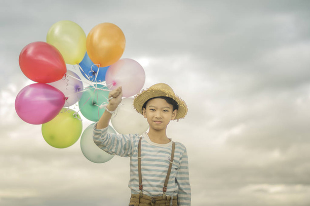 Cute asian boy holding colored balloons on cloudy sky background. - Zdjęcie, obraz