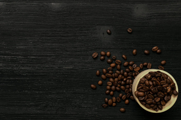 Kaffeebohnen im Holztopf und verstreute Kaffeebohnen isoliert auf schwarzem Holztischhintergrund mit Kopierraum. Kaffeezeit. - Foto, Bild