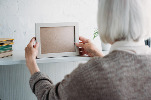 partial view of senior lady taking empty photo frame from bookshelf at home - Valokuva, kuva