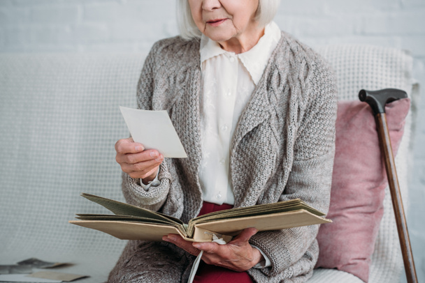 Schnappschuss von Seniorin mit Fotoalbum, die zu Hause auf Couch sitzt - Foto, Bild