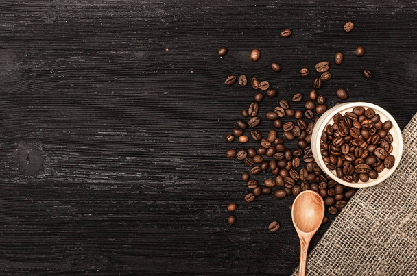 Coffee beans scattered from a wooden pot full of coffee and wooden spoon on black table surface background with copy space. - Foto, afbeelding