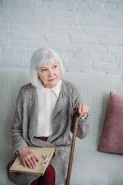 Nachdenkliche Seniorin mit Fotoalbum ruht zu Hause auf Couch - Foto, Bild