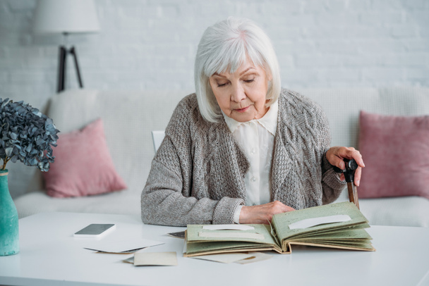 portrait  of grey hair woman looking at photos in photo album at table at home - Photo, Image