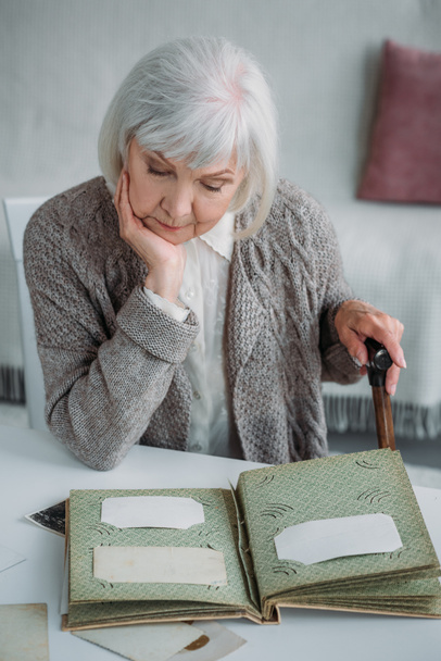 portrait of grey hair woman looking at photos in photo album at table at home - Photo, Image