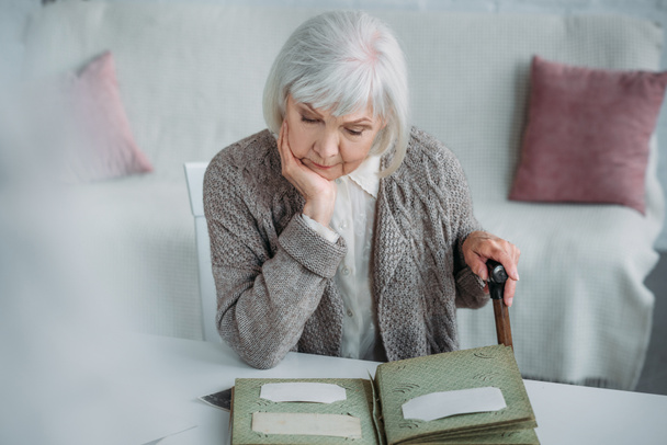 portrait of grey hair woman looking at photos in photo album at table at home - Photo, Image