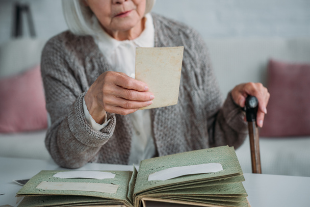 częściowy widok starszy Kobieta, patrząc na zdjęcie z albumu fotograficznego przy stole w domu - Zdjęcie, obraz