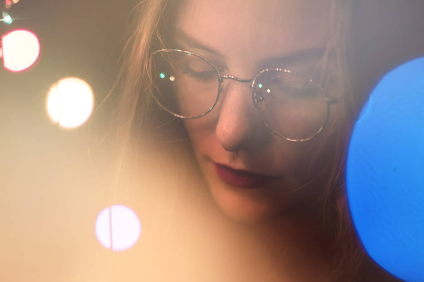Portrait of a fashion beautiful white girl with glasses in the dark and bokeh Orange tinting. Effect of the focus of the low intensity of sharpness. Light toning - Photo, Image