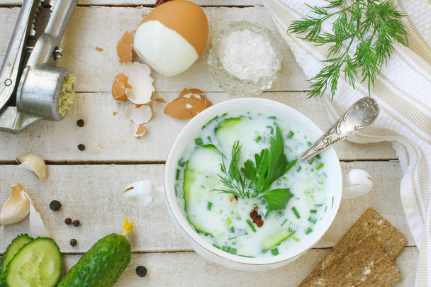 cold yogurt soup with cucumber, herbs, boiled egg and garlic in a white bowl on a wooden table - Foto, Imagen