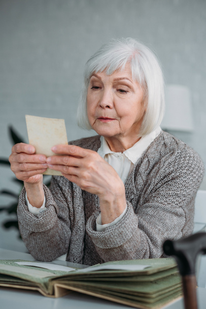 portrait of grey hair woman looking at photo from photo album at table at home - Photo, Image