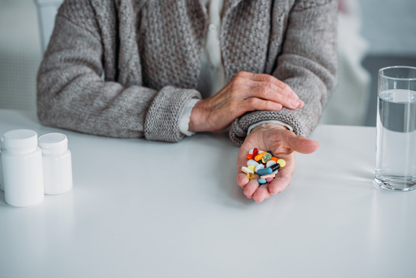 cropped shot of senior woman with pills in hand sitting at table alone at home - Фото, зображення