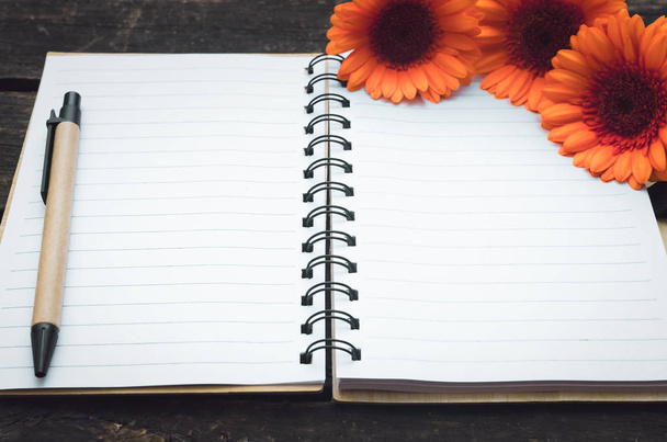 Blank page notepad and orange gerbera flowers on wooden background. - Фото, изображение