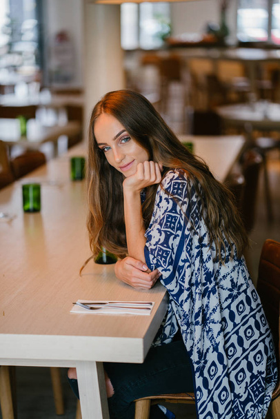 Portrait of young attractive woman with long hair sitting in cafe and looking at camera - Foto, Imagen