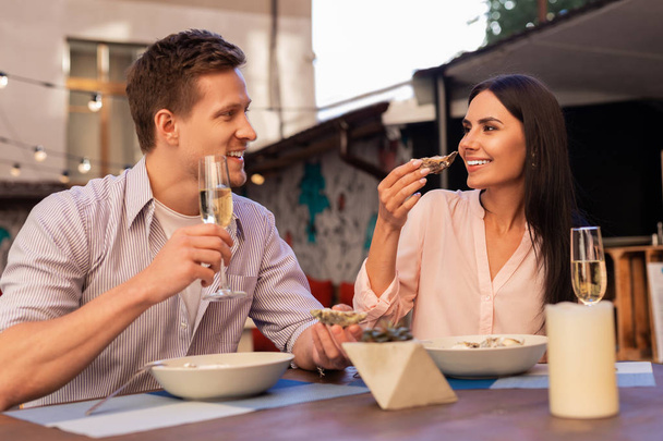Mies yllään raidallinen paita ottaa samppanjaa ja syö ostereita vaimonsa kanssa
 - Valokuva, kuva