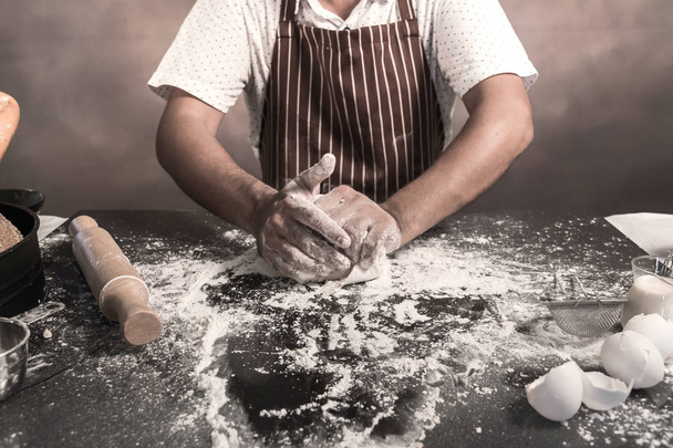 Man preparing buns at table in bakery, Man sprinkling flour over fresh dough on kitchen table - Foto, Imagen