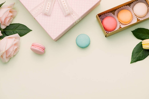 Colorful macaroons and rose flowers with gift box on light green. Sweet macarons in gift box. Top view - Fotoğraf, Görsel