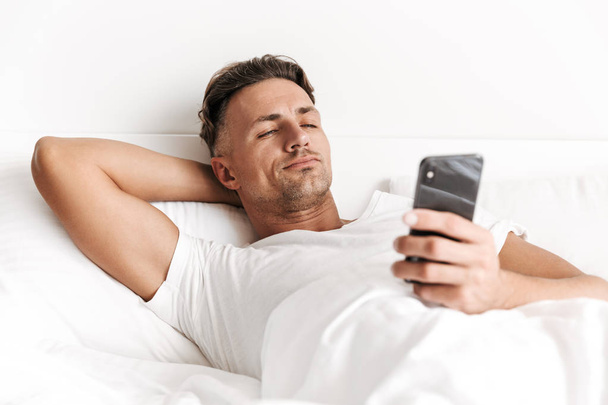 Handsome man using mobile phone while laying in bed - Foto, Imagem