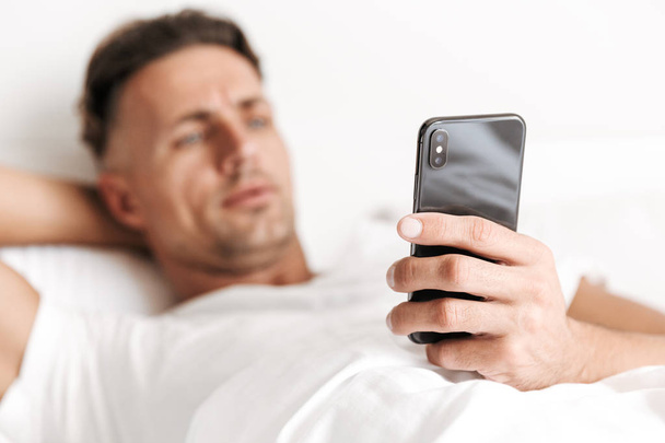 Lähikuva komea mies käyttää matkapuhelinta makaamassa sängyssä
 - Valokuva, kuva