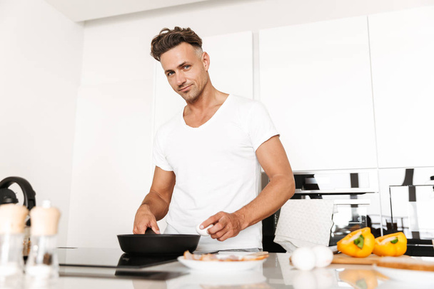 Smiling man cooking eggs for breakfast while standing at a kitchen - Foto, Imagen