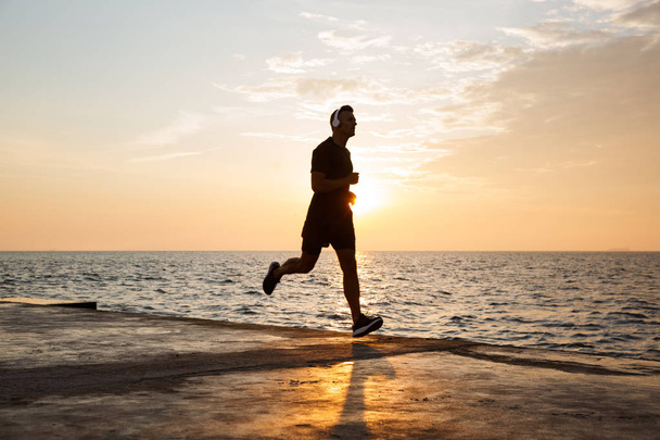 Full length of a confident sportsman with headphones running along the beach - Foto, Imagem