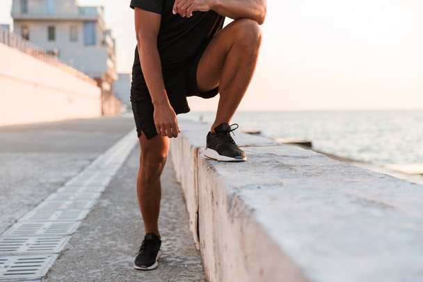 Cropped image of sportsman with headphones doing stretching exercises at the beach - Φωτογραφία, εικόνα