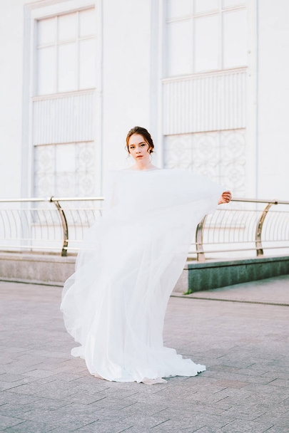Ευτυχισμένος νεαρή νύφη στο ρέοντας λευκό φόρεμα απολαμβάνοντας τον εαυτό της σε εξωτερικούς χώρους - Φωτογραφία, εικόνα