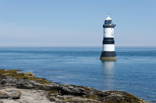 Penmon lighthouse in Anglesey on a bright, sunny, summers day with some shoreline in view. - Photo, Image