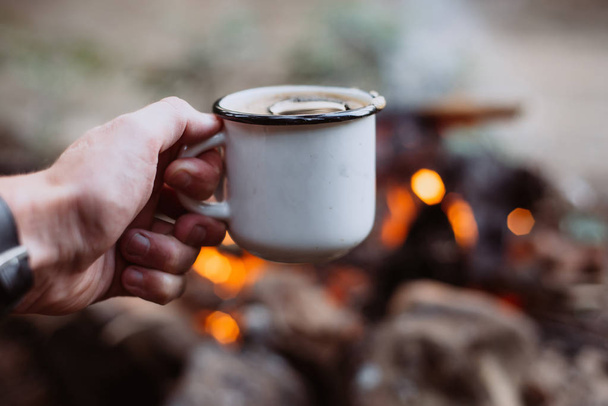 Coffee in the hands of the background of the fire at a summer camp. - Fotoğraf, Görsel