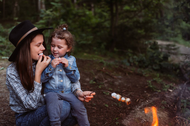 mother and daughter roast marshmallow candies on the campfire in forest. Spring or autumn camping - Фото, зображення