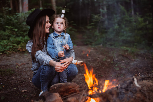 mother and daughter roast marshmallow candies on the campfire in forest. Spring or autumn camping - Foto, immagini