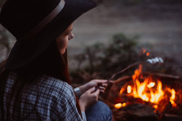 Traveler girl fry marshmallows on fire in the woods. Evening light. - Foto, afbeelding