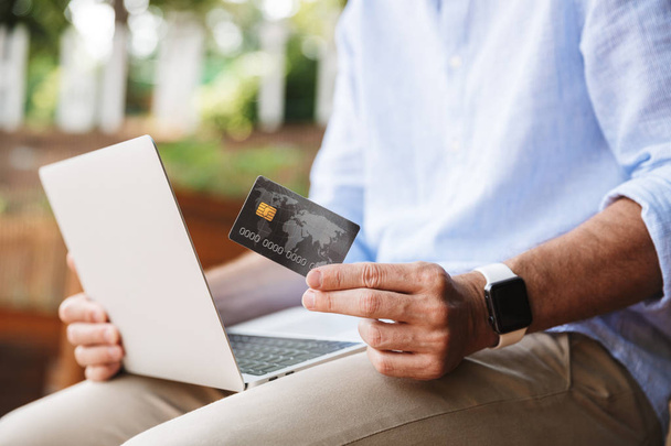 Cropped photo of man outdoors using laptop computer holding credit card. - Foto, immagini