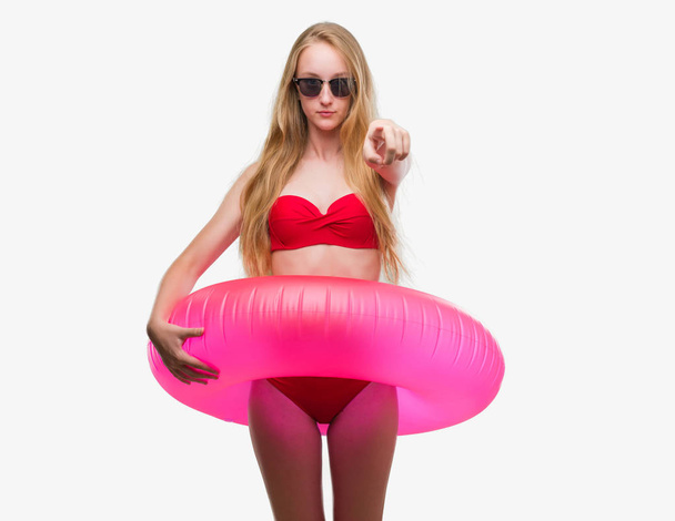 Bionda adolescente che indossa bikini e tiene il galleggiante rosa puntato con il dito verso la fotocamera e verso di te, segno della mano, gesto positivo e fiducioso dal davanti
 - Foto, immagini