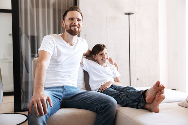 Image of shocked young man father dad having fun with his son indoors at home watching TV. - Φωτογραφία, εικόνα