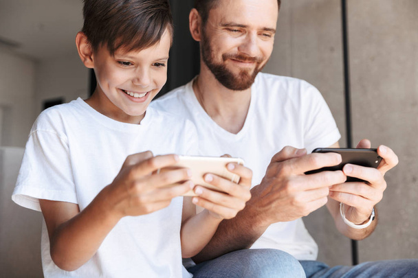 彼の息子の子供と自宅屋内でハンサムなひげを生やした男の画像は携帯電話でゲームをプレイします。. - 写真・画像