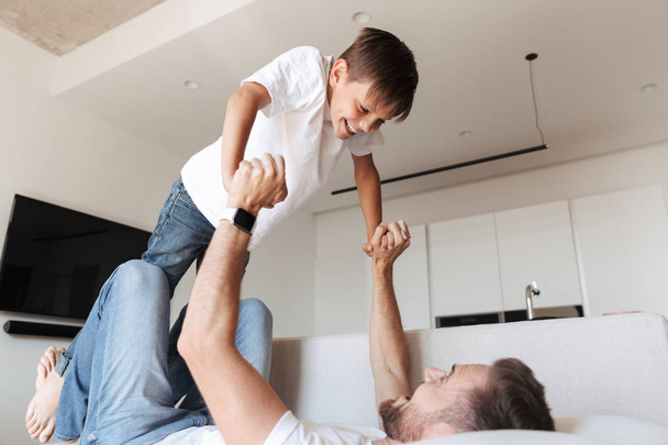 Image of handsome bearded man indoors at home with his son child having fun. - Foto, Bild