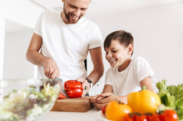 Photo of cheerful young man father dad cooking with his son indoors at home in kitchen. - Foto, Bild