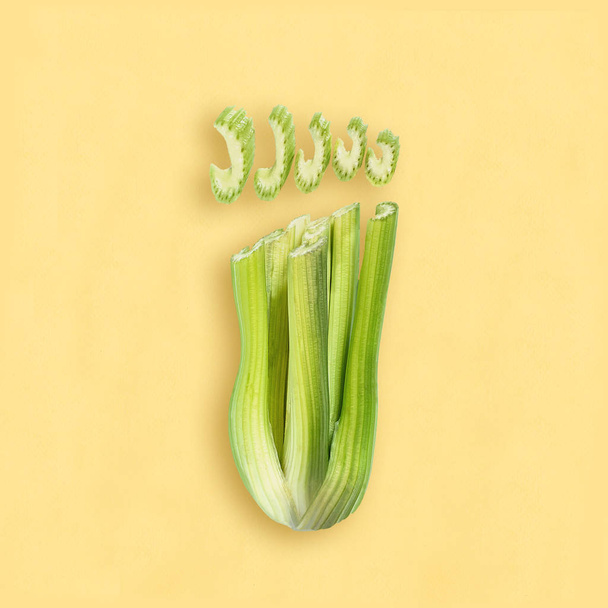 Fresh stems and celery pieces in form of foot on pastel lilac background. Minimal style. Fitness concept. Dietary and healthy food - Photo, image