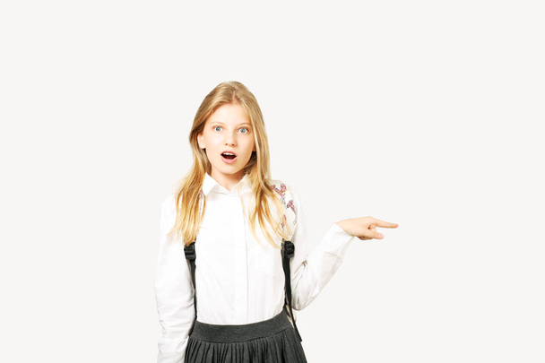 Close up portrait, young beautiful happy teenage school girl surprised, astonished, standing on white background looking pointing to side copy space with index finger. Back to school sale concept. - Foto, Bild