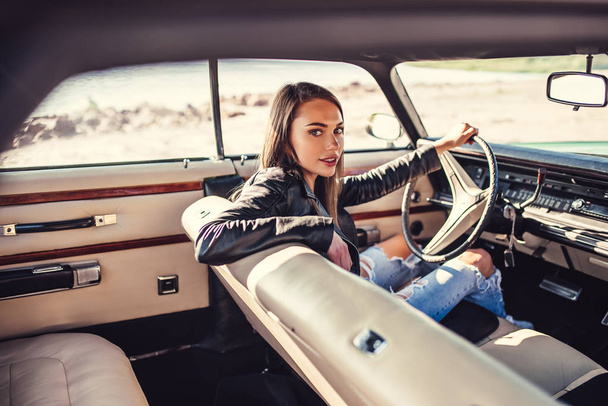 Attractive young woman is sitting in green retro car on the beach. Vintage classic car. - Foto, Imagen