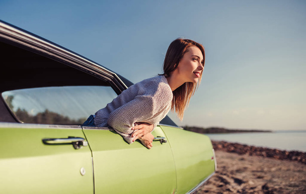 Почувствуйте дух приключений! Привлекательная молодая женщина высовывается из окна зеленого ретро-автомобиля. Винтажный классический автомобиль
. - Фото, изображение