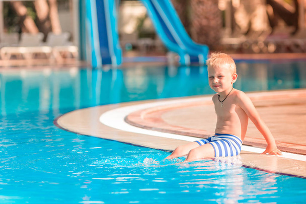 Милий маленький хлопчик сидить на краю басейну
 - Фото, зображення