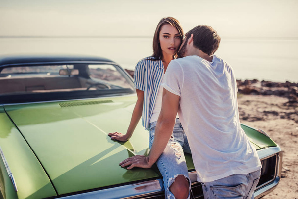 Romantic couple is standing near green retro car on the beach. Handsome bearded man and attractive young woman with vintage classic car. Love story. - Φωτογραφία, εικόνα