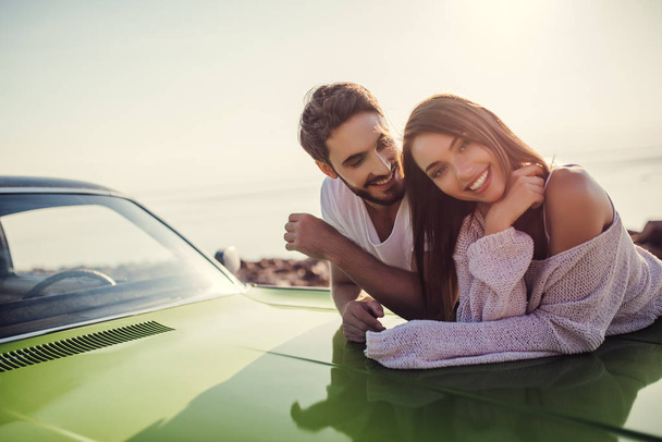 Romantic couple is standing near green retro car on the beach. Handsome bearded man and attractive young woman with vintage classic car. Love story. - Photo, Image