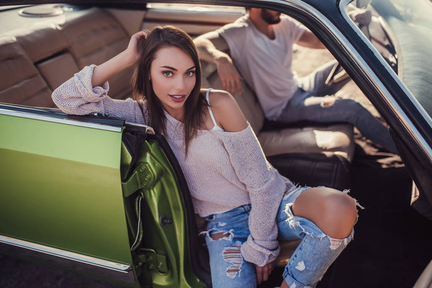 Romantic couple is sitting in green retro car on the beach. Handsome bearded man and attractive young woman in vintage classic car. Stylish love story. - Foto, imagen