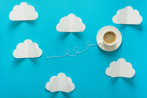 Coffee cup in shape of balloon with clouds on blue paper background. - Photo, image